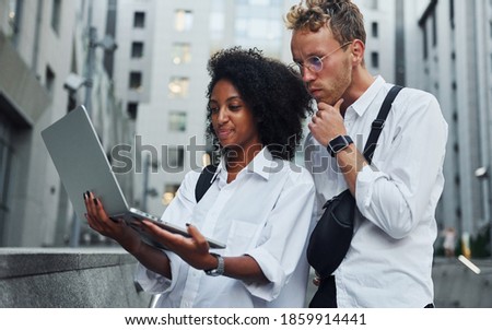 Uses laptop. Man with afrian american woman together in the city outdoors.