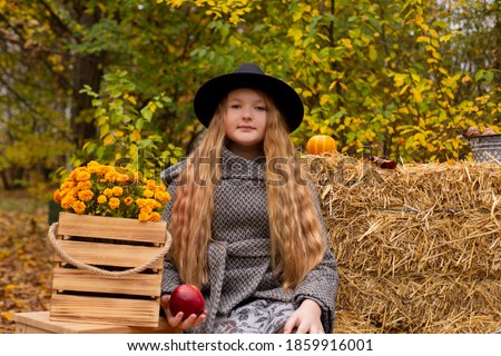 cute brunette teen girl in black hat and gray coat near autumn elements decoration - pumpkins, apples, plaid, hay. Cosiness, autumn.