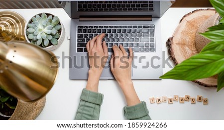 Workplace at home. Laptop, plants and wooden lettering: "Freelance" on a white table. Start of the working day in quarantine. The concept of human resource management, recruitment and recruitment. Royalty-Free Stock Photo #1859924266