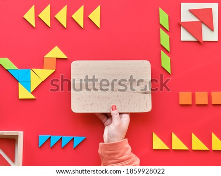 Creative design for Autism World Day on April 2. Tangram elements scattered and arranged in pictogram on red background. Hand hold wooden board with text space, copy-space.