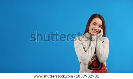 Young woman in Christmas sweater on blue background, space for text