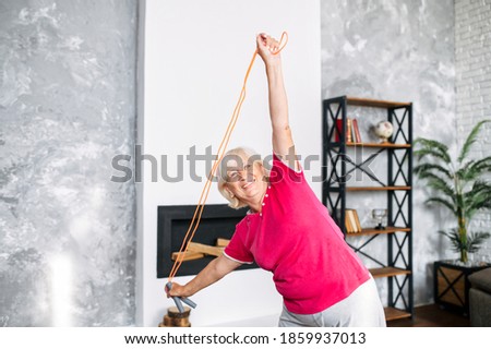 Healthy and cheerful aging woman doing sports exercises in living room at home. A grandmother with skipping rope