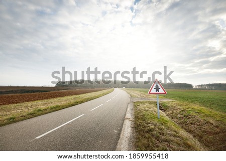 An empty asphalt road (highway) through the fields, street sign close-up. Dramatic sky. France, Europe. Transportation, logistics, travel destinations, tourism, driving, speed, freedom, lockdown