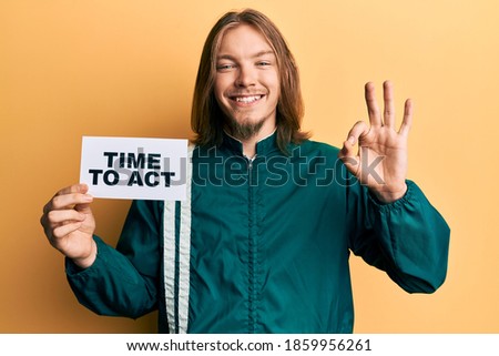 Handsome caucasian man with long hair holding time to act banner doing ok sign with fingers, smiling friendly gesturing excellent symbol 