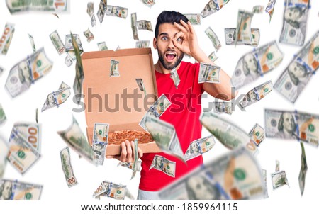 Young handsome man with beard holding delivery cardboard with italian pizza smiling happy doing ok sign with hand on eye looking through fingers