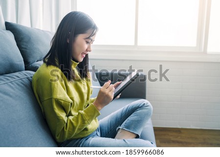 Beautiful Asian happy smile woman using tablet technology playing entertainment internet browsing social media website studying business, in free time domestic home lifestyle comfy in living room 