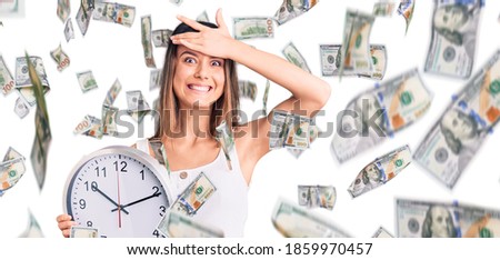 Young beautiful girl holding big clock stressed and frustrated with hand on head, surprised and angry face