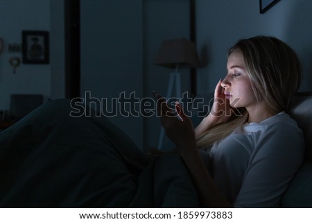 Sleepy exhausted young woman lying in bed using smart phone, chatting and bored, can not sleep. Insomnia, nomophobia, sleep disorder concept. Social media addiction Royalty-Free Stock Photo #1859973883