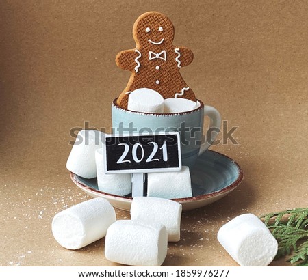 Gingerbread man in a cup with marshmallows on craft background with 2021 chalkboard 
