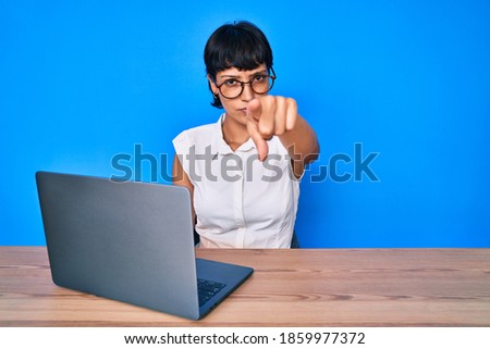 Beautiful brunettte woman working using computer laptop pointing with finger to the camera and to you, confident gesture looking serious 