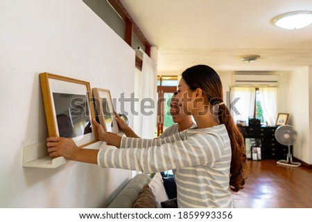 Young couple hanging picture frame on wall in their new house. Smiling husband and wife happy settling together in newly owned home Royalty-Free Stock Photo #1859993356