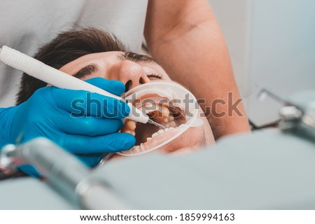 Dental practice, the dentist removes stones and hard plaque from the teeth with the help of ultrasound,patient with retractor and saliva ejector in the mouth. Royalty-Free Stock Photo #1859994163