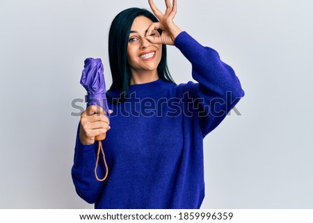 Young caucasian woman holding purple closed umbrella smiling happy doing ok sign with hand on eye looking through fingers 