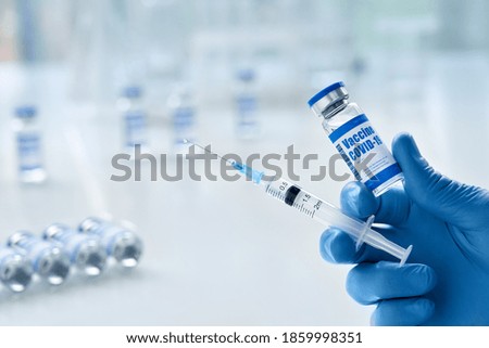 Male doctor hand wears medical glove holding syringe and vial bottle with covid 19 corona virus vaccine drug multiple dose for injections. Coronavirus cure, flu medicine treatment vaccination concept. Royalty-Free Stock Photo #1859998351
