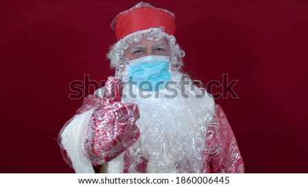 Russian santa claus in a medical mask on a red background shows thumbs up