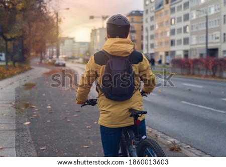 A man, wearing a winter jacket, cycling in the city. Royalty-Free Stock Photo #1860013603