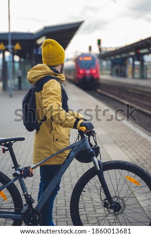 Vertical Photo of a man in winter clothes, waiting with his bike, the train. In the background the train that is about to arrive. Royalty-Free Stock Photo #1860013681