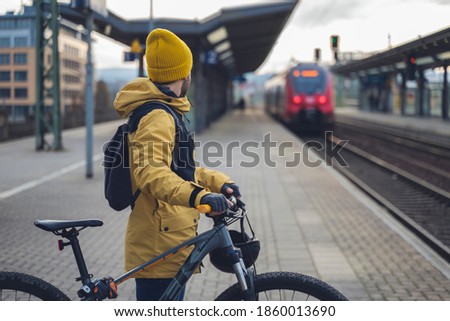 A man in winter clothes, waiting with his bike, the train. In the background the train that is about to arrive. Royalty-Free Stock Photo #1860013690