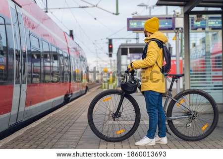 A man, wearing winter clothes, at the station, is about to get on the train, with his bicycle. Royalty-Free Stock Photo #1860013693