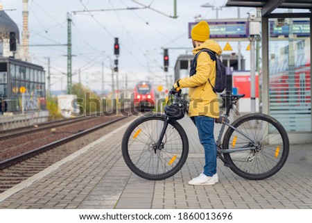 A man in winter clothes, waiting with his bike, the train. In the background the train that is about to arrive. Royalty-Free Stock Photo #1860013696