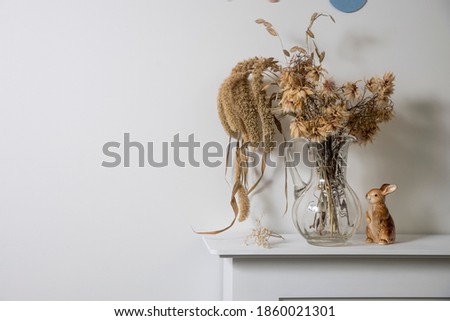 Dried flowers Nigella damascena and cereals in a transparent glass decanter stand on a white console in a Scandinavian interior. Square frame. Copy space