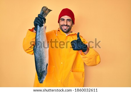 Handsome hispanic man with beard wearing fisherman equipment smiling happy and positive, thumb up doing excellent and approval sign  Royalty-Free Stock Photo #1860032611