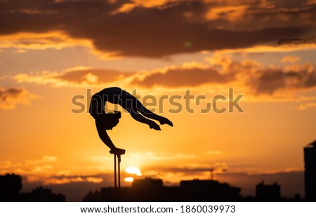 Flexible female circus Artis keep balance and doing contortion on the rooftop against dramatic sunset and cityscape. Handstand and equilibrium concept 