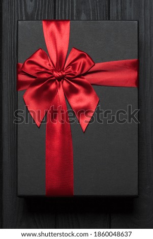 Black gift box with red big bow on a wooden surface. Photo of a 