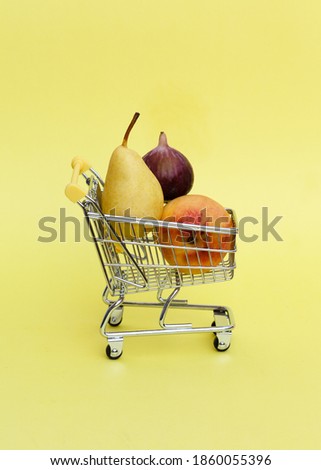 Shopping trolley with few fruits on pastel yellow background. Vertical shot, copy space. Shopping of vegetarian diet products. Trendy sale minimal concept.