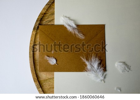 Blank white card mockup and envelope on round wooden platewhite feathers and white grass in background. Modern template. Branding identity. Natural autumn, fall design. Flat lay, top view