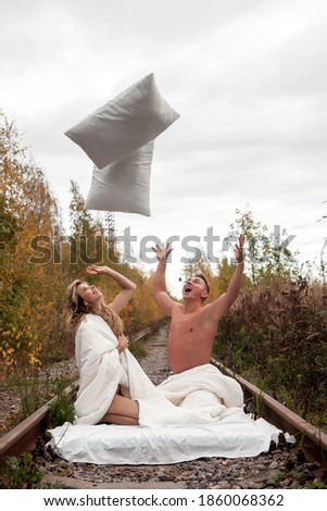 Young cute couple throw pillows up in bed on train tracks, symbolizing freedom of borders and permits of travel after pandemic. Concept of romantic travel ban and love story. Stay at home. Copy space
