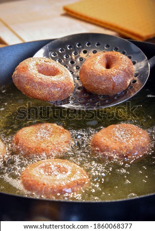 Freshly made donuts coming out of the frier pan and some still cooking in the hot oil. Royalty-Free Stock Photo #1860068377