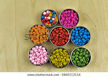Small, colorful, wooden beads in metal containers.