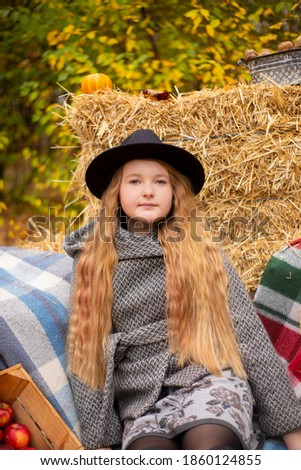 cute brunette teen girl in black hat and gray coat near autumn elements decoration - pumpkins, plaid, hay. Cosiness, autumn. 