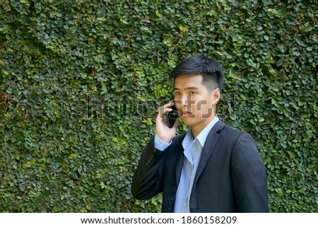 Young Asian businessman walking in the park using a smart phone.