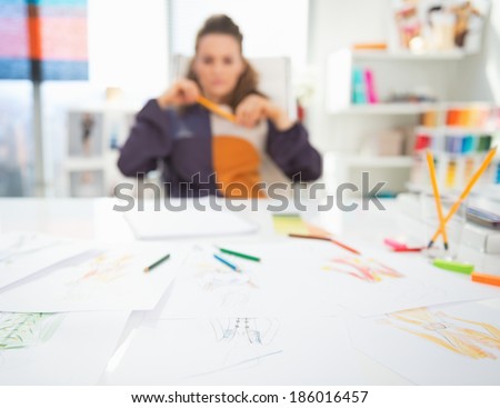 Closeup on table and thoughtful fashion designer in background