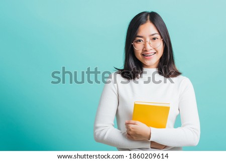 Portrait female in glasses is holding the books on hand, Young beautiful Asian woman hugging books, studio shot isolated on a blue background, Education concept