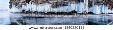 A panoramic view of icy rocks and reflection in the smooth ice on a winter day. Beautiful landscape of frozen Lake Baikal. Natural background, panorama, banner