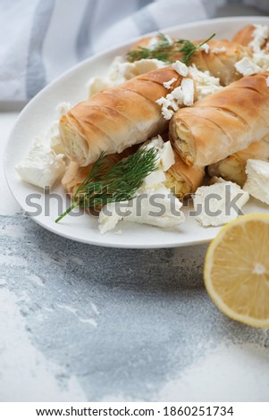 Closeup of greek baked mini filo rolls filled with feta cheese, vertical shot on a white concrete surface