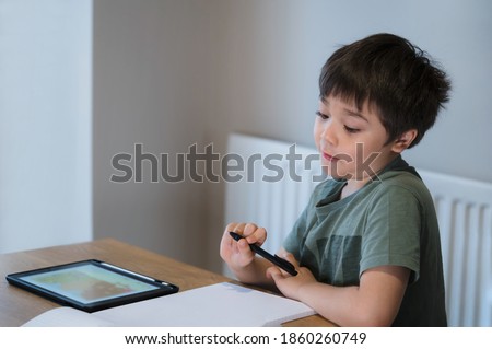 Candid shot kid using tablet for his homework,Child boy  making surprise face while doing homework by using digital tablet searching information on internet,E-learning,Home schooling education concept