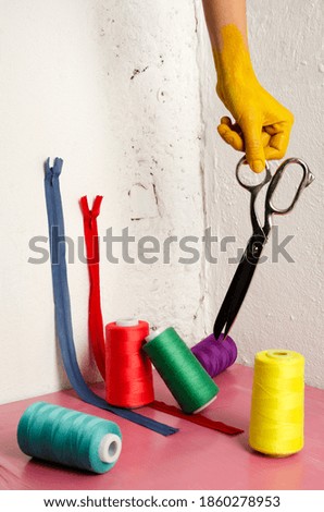 Vertical image.Colored woman hand, scissors, assortment of different colors of thread,zippers on the pink surface against white wall