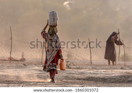 shepherd woman carrying water on her head for family in traditional dress walking on the ground , nomadic life of koochi  from Baluchistan 