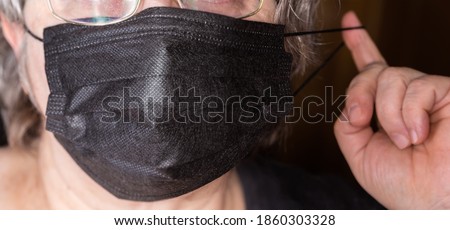 Black disposable three-ply protective mask with rubber bands while dressing on the women face, fragment close-up in selective focus
