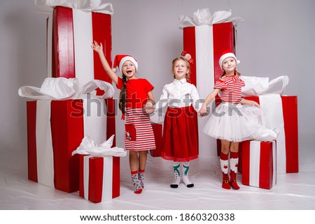 funny little girs lfriends in Christmas costumes against the background of big red presents. idea and concept of a happy holiday, new year, friendship and childhood.