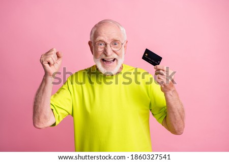 Photo of old happy excited cheerful grandfather wear lime t-shirt raise fists hold credit card isolated on pink color background