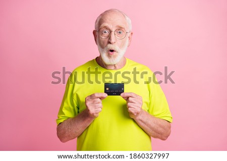 Photo of old shocked surprised grandfather wear lime t-shirt hold credit card isolated on pink color background