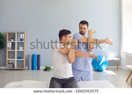Joint motion recovery. Physiotherapist teaching male patient to do arm across chest or cross-body stretch exercise to relieve shoulder pain, cure frozen shoulder and help get rid of joint stiffness Royalty-Free Stock Photo #1860342079