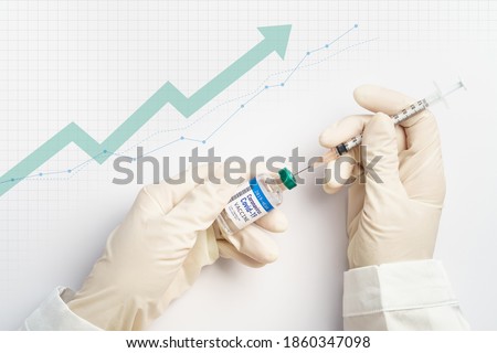 Global economy recovery after Covid 19 concept. Hands of a researcher in medical gloves takes shot from Coronavirus Vaccine vial by needle syringe with stock index chart rising up in the background. Royalty-Free Stock Photo #1860347098