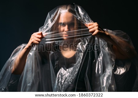 Woman freedom. Female rights. Feminist empowerment. Art portrait of furious mad angry trapped lady tearing off breaking through clear polyethylene film bag isolated on dark background.