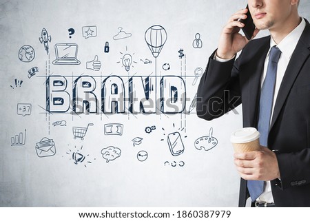 Unrecognizable businessman with coffee talking on phone near concrete wall with creative brand sketch drawn on it